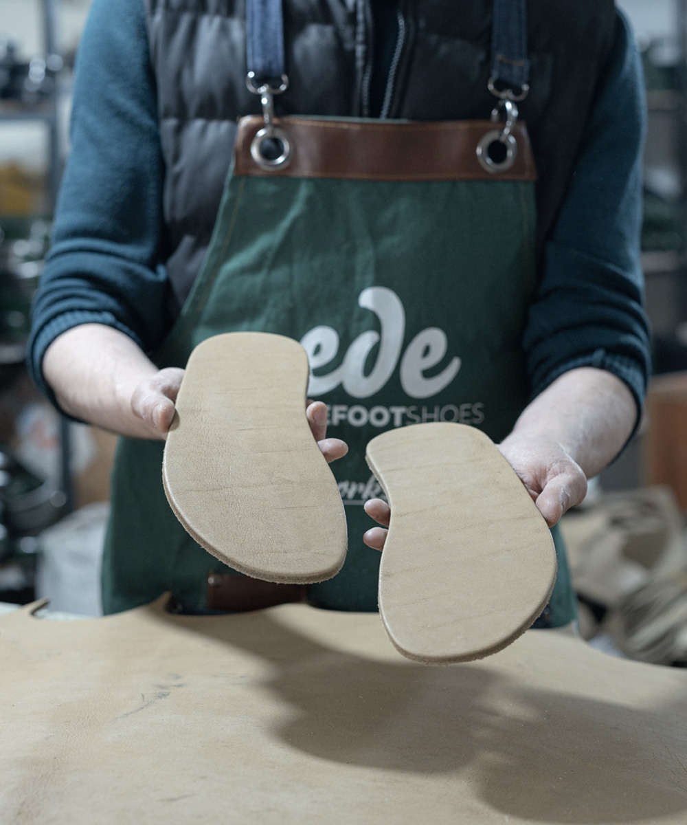 Craftsman holding hand-cut buffalo leather soles in the Ede atelier